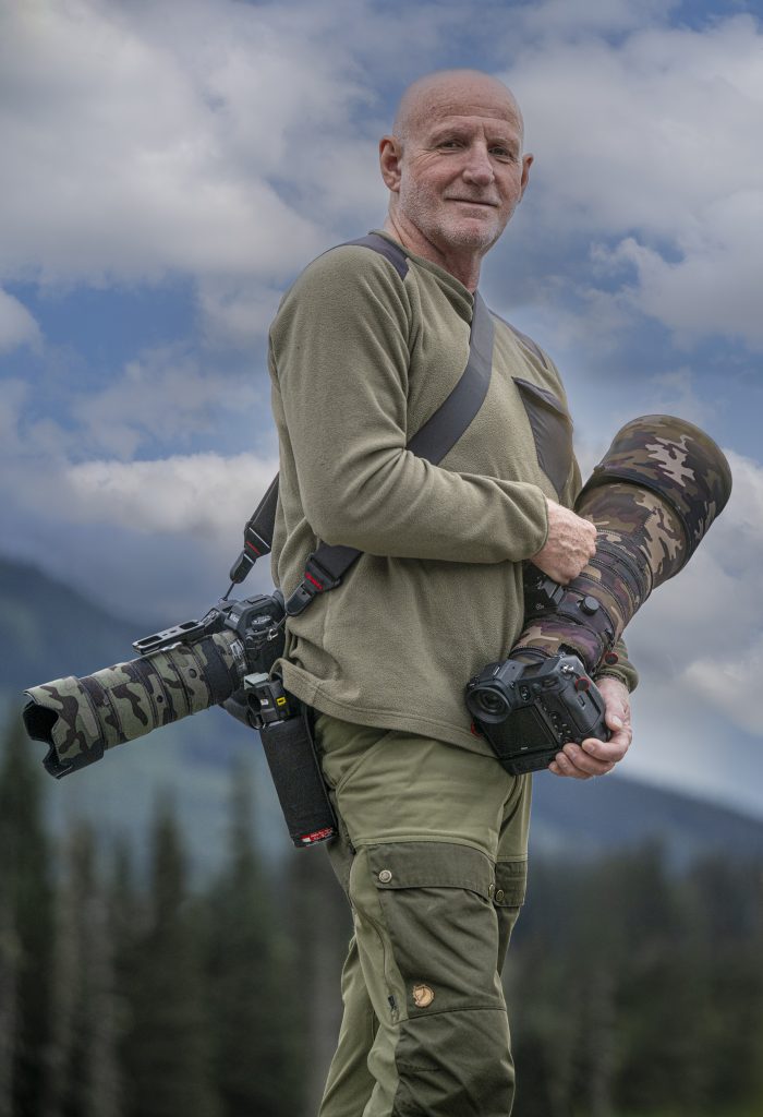 Le photographe Gilles Thomas portant son boîtier équipé d'un téléobjectif sur l'épaule.