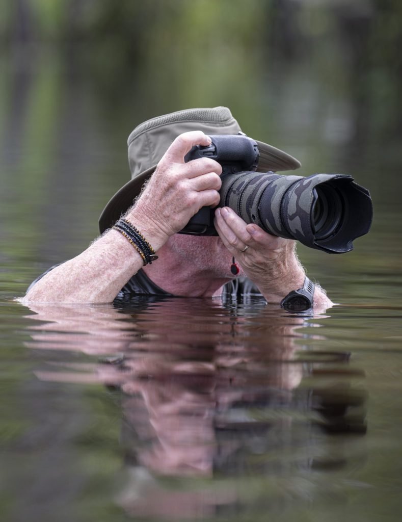 Le photographe animalier Gilles Thomas camouflé et immergé dans l'eau, concentré derrière son objectif.